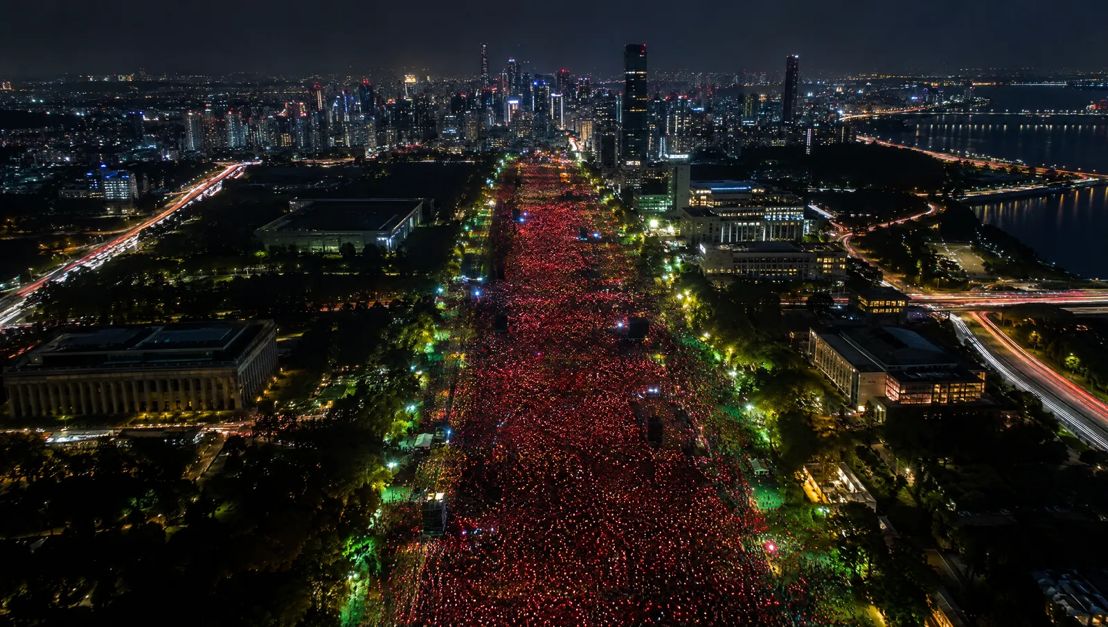 Vista aérea noturna de uma avenida tomada por milhares de pequenas luzes vermelhas